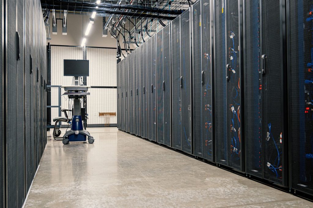 Armários metálicos com servidores, equipamentos de rede e cabos em uma sala moderna de data center.