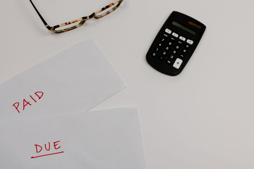 Documentos financeiros identificados como pagos e pendentes ao lado de uma calculadora e óculos.