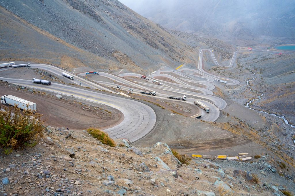 Vista aérea de uma estrada sinuosa em região montanhosa do Chile, com caminhões de carga circulando