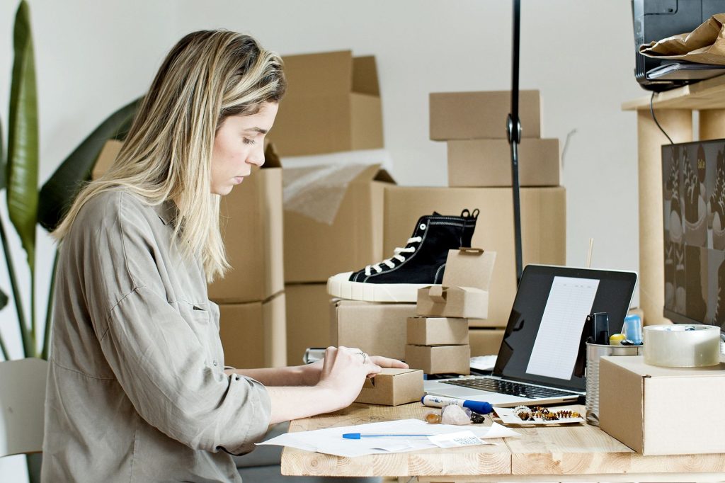Brasil atinge recorde, mas só 35% dos empreendedores tinham CNPJ em 2025, aponta IBGE Mulher prepara caixas para uma loja on-line, cercada por materiais de embalagem e um laptop.