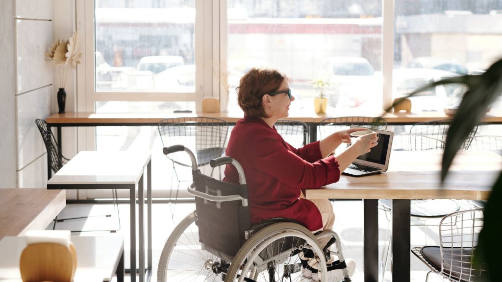 Mulher em cadeira de rodas trabalha em um laptop em um café.