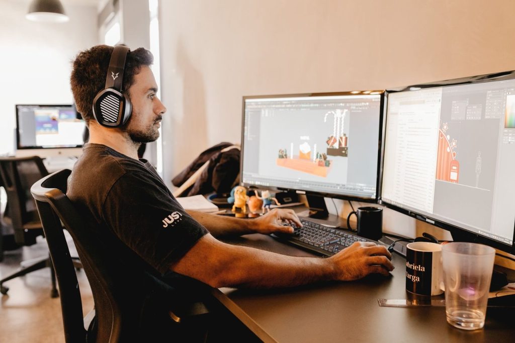 Profissional usando fones de ouvido diante de dois monitores em um escritório moderno.