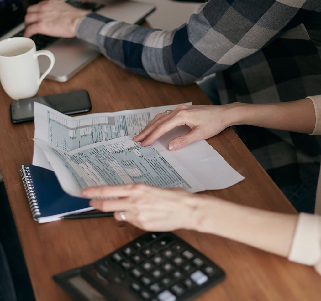 Prospera MEI: o que pode mudar para quem tem dívidas e busca investir no negócio Mãos organizam documentos fiscais sobre uma mesa com calculadora, notebook e caderno.